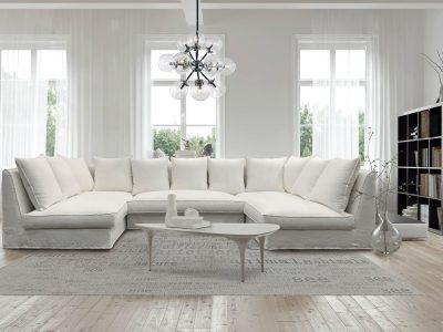 Modern spacious lounge or living room interior with monochromatic white furniture and decor below three tall bright windows with a dark bookcase accent in the corner